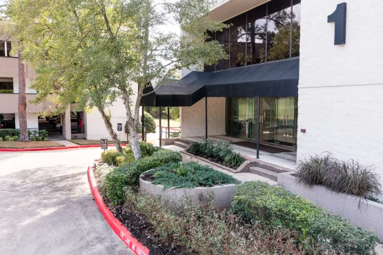 Entrance to Building 1 with a black awning, glass doors, and landscaped grounds.