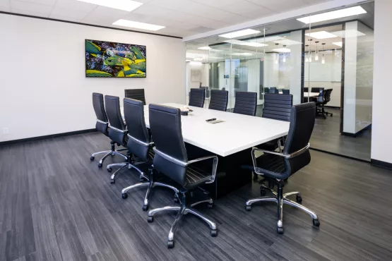Spacious conference room with a white table, black leather chairs, and glass partition walls.