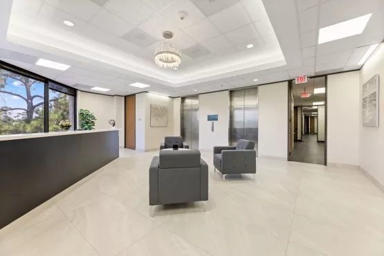 Office building lobby with reception desk, gray chairs, and elevators