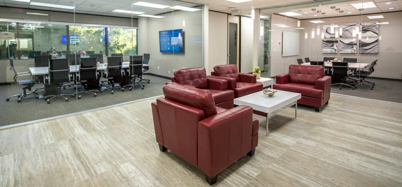 A modern Avalon Suites common area featuring red leather lounge seating, a white coffee table, and glass-walled conference rooms on either side.