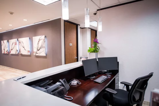 The Avalon Suites front desk area featuring dual monitors, business phones, pendant lighting, a fresh floral arrangement, and decorative abstract artwork along a dark accent wall.