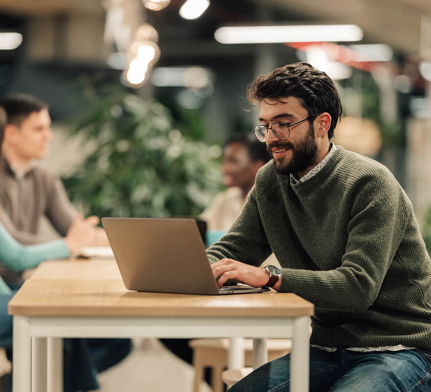 Freelancer working on laptop at shared desk in coworking space with other professionals in background