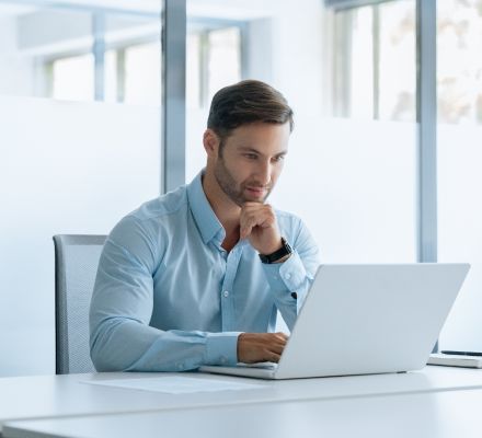 Man working on a laptop at a white desk in a bright office.
